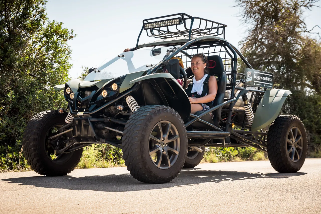 Two smiling people in a green two-seater road buggy on a paved road