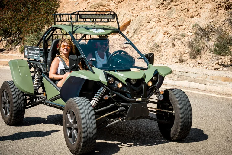 Two people in a green road buggy on a paved road below a rock face