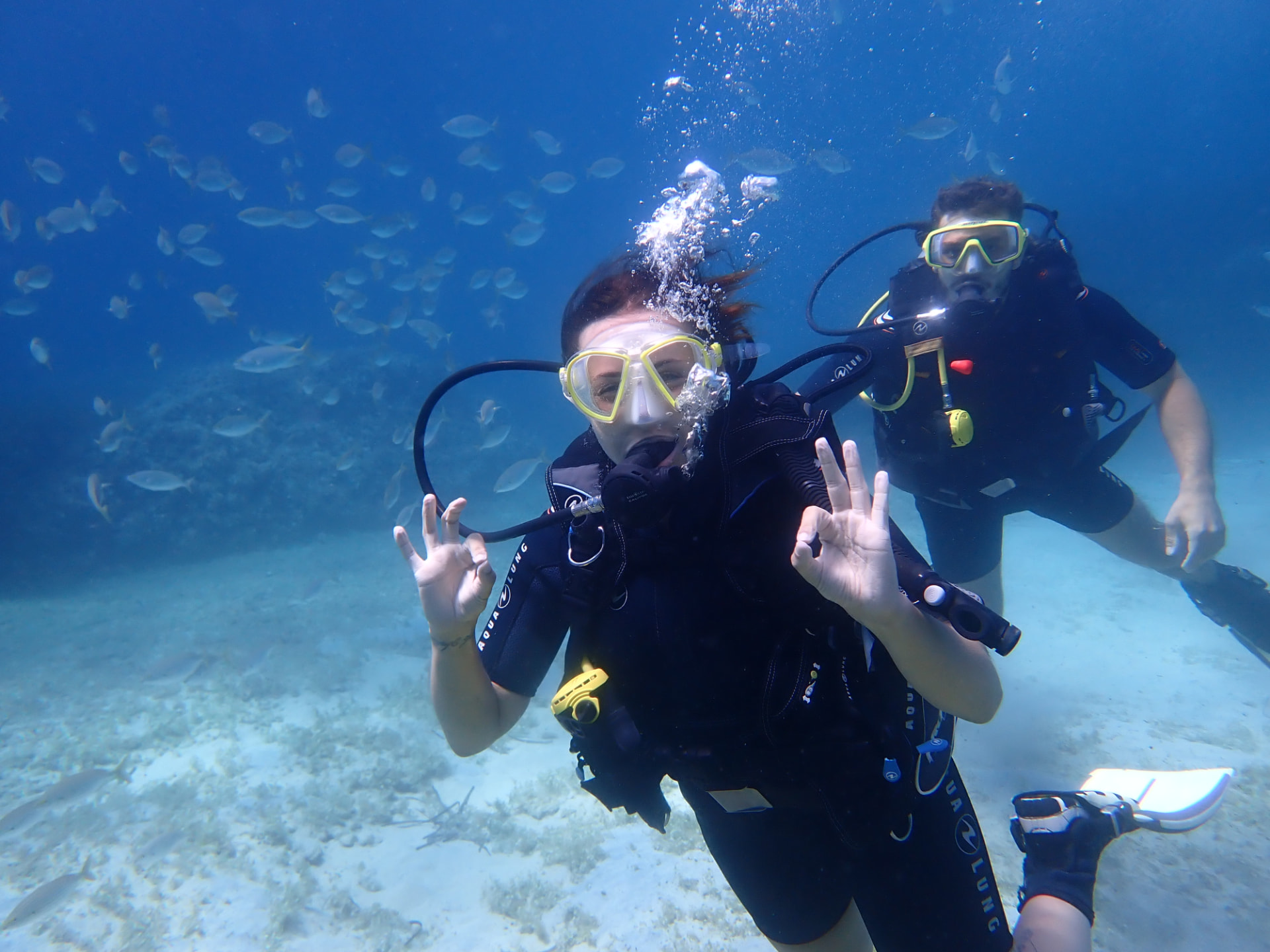 Diver underwater giving two OK signals with another diver close behind