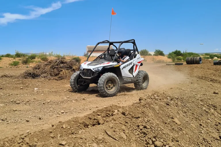 Child with helmet driving a white kids buggy on a dirt circuit
