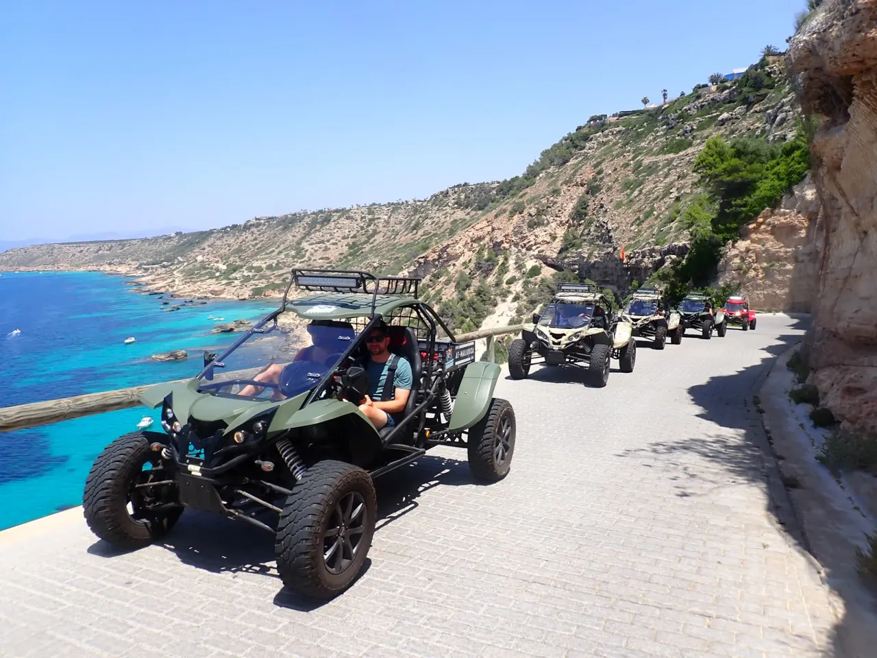 Road buggies in a line on a coastal road above turquoise sea