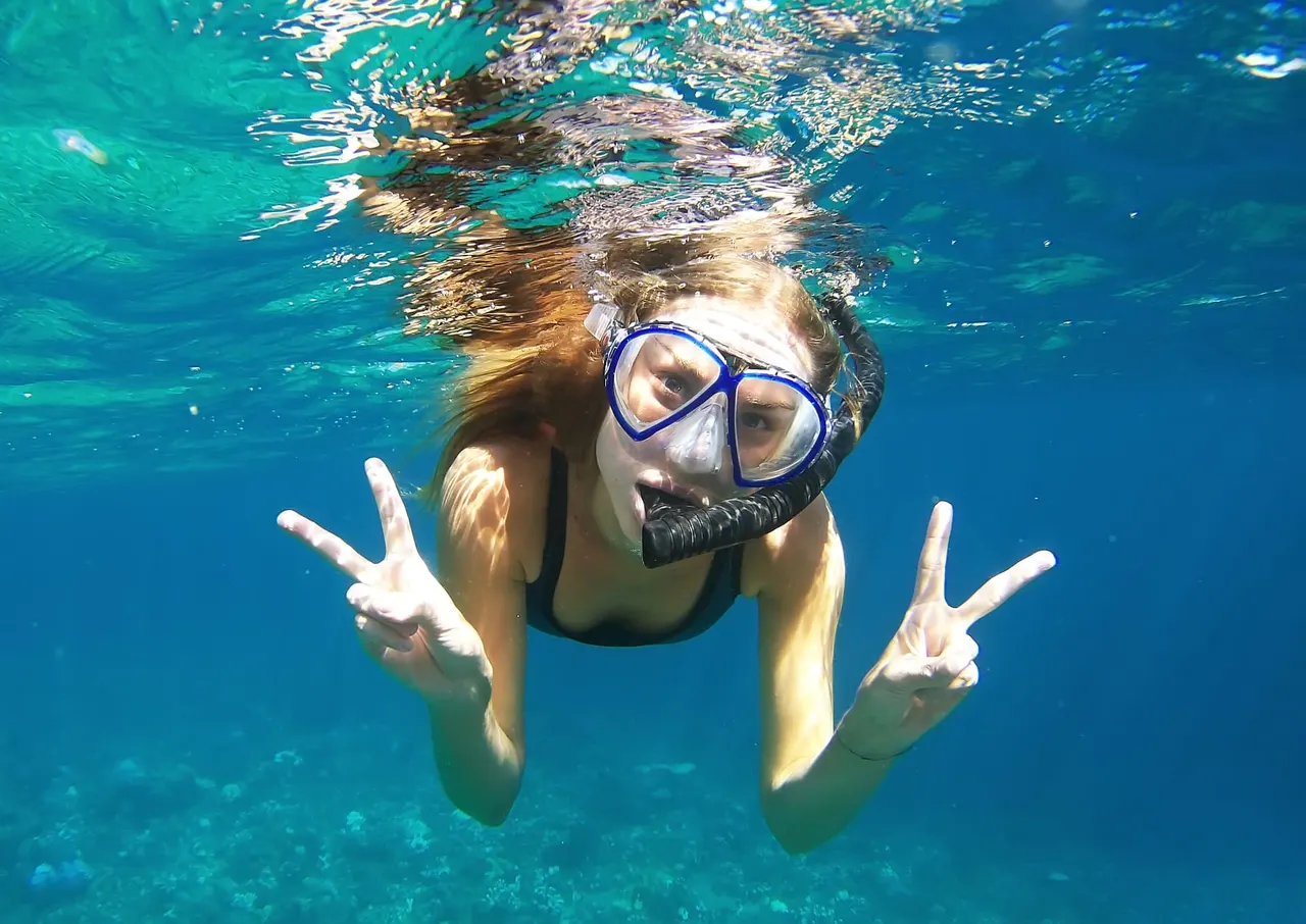 Snorkeler with mask and snorkel just below the water surface, making peace signs with both hands