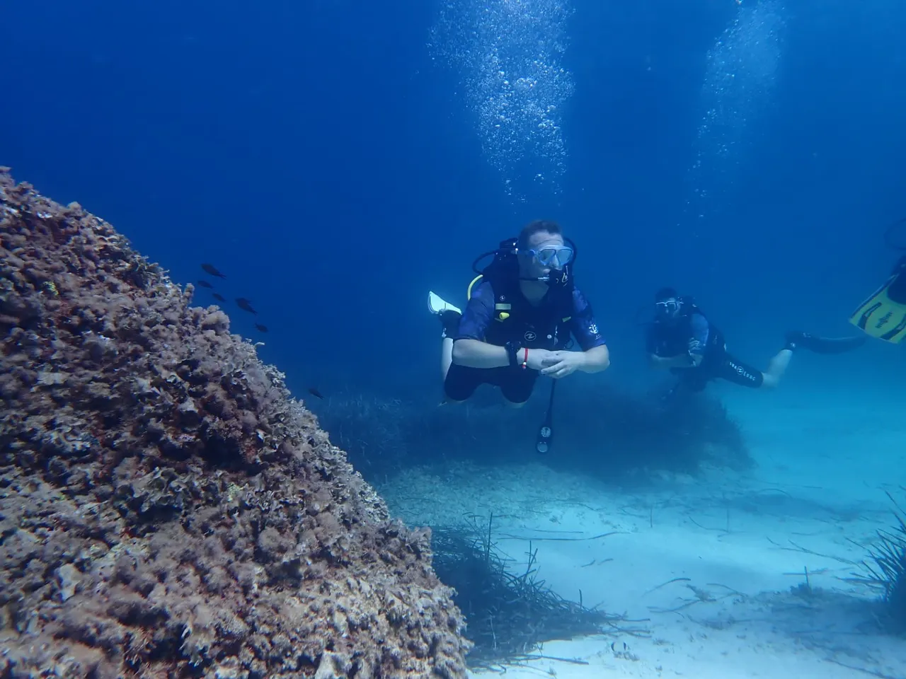Certified divers following their guide past a rock formation off Mallorca