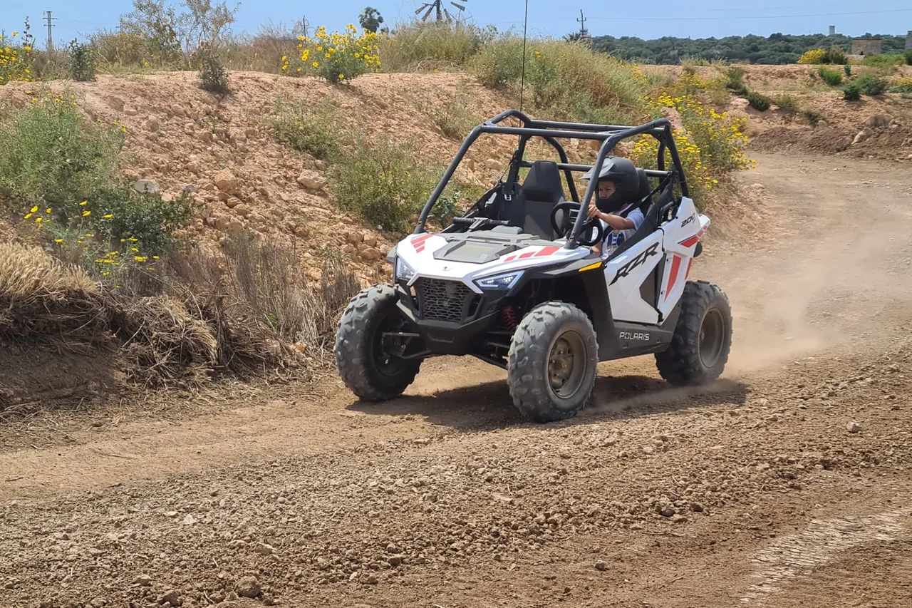 Child with helmet driving a white kids buggy on a dirt track
