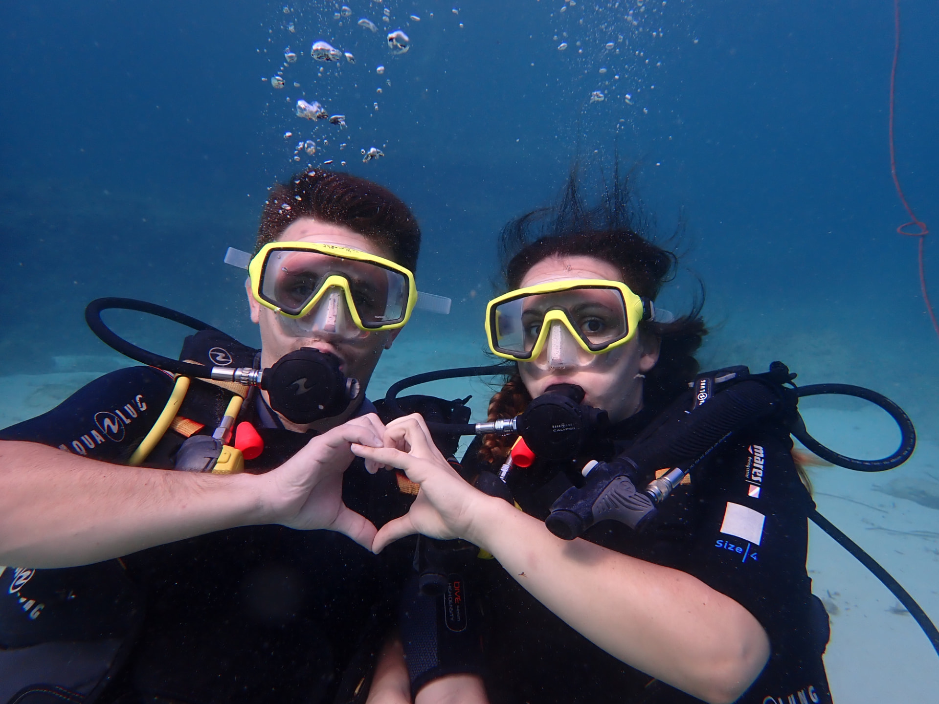 Two divers underwater forming a heart shape with their hands
