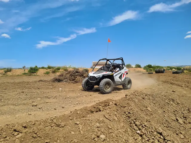 White kids buggy on the dirt circuit under a blue sky, with tyre stacks at the edge