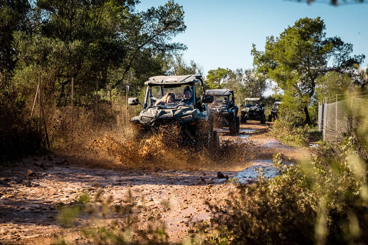 Group of buggies driving along a muddy track, spraying mud, two smiling people in the front buggy