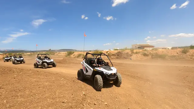 Kids buggy with two helmeted people in front, more buggies following on the dirt circuit